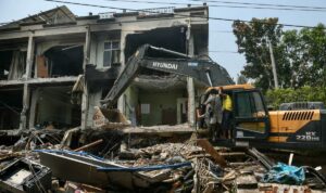 Alat berat konstruksi digunakan untuk menggali reruntuhan saat orang-orang mencari korban selamat di sebuah bangunan yang rusak